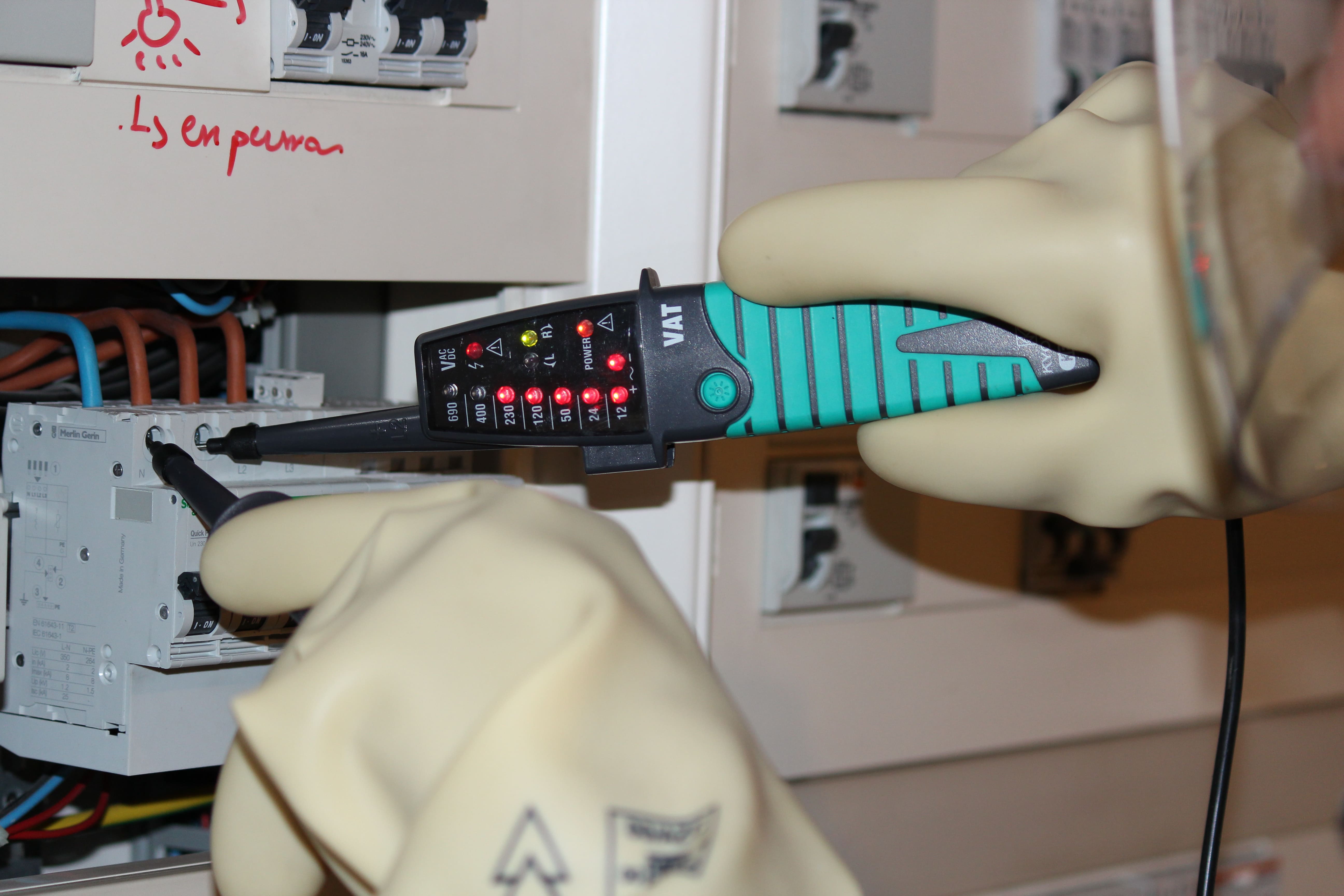 testeur-electrique-utilisation Technicien utilisant un testeur électrique avec gants isolants.
